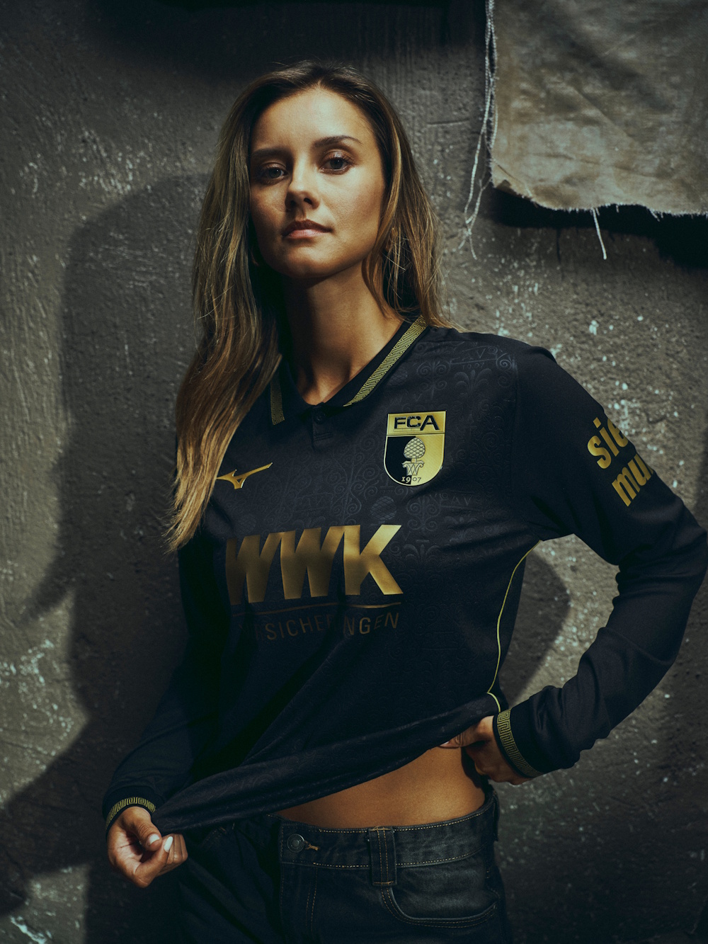 Model Nikola trägt das schwarz-goldene Römertrikot des FC Augsburg für die Saison 2025/26